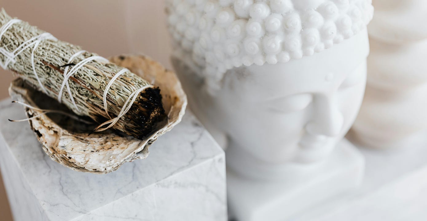 Smudge stick sitting on a shell next to a white marble budha